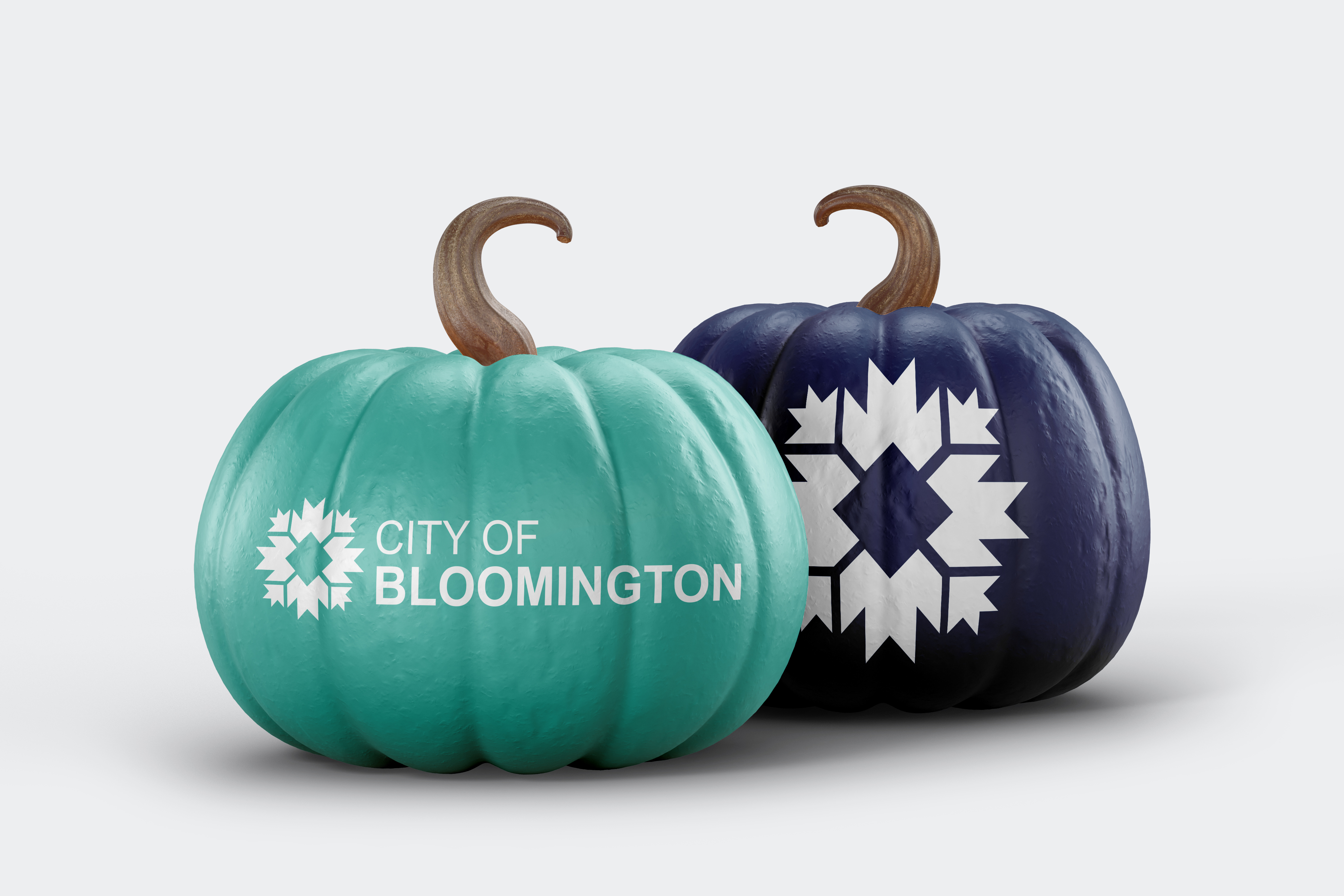 A teal pumpkin sitting next to a navy blue pumpkin on a light gray background. Both pumpkins showcase the city logo in whote.