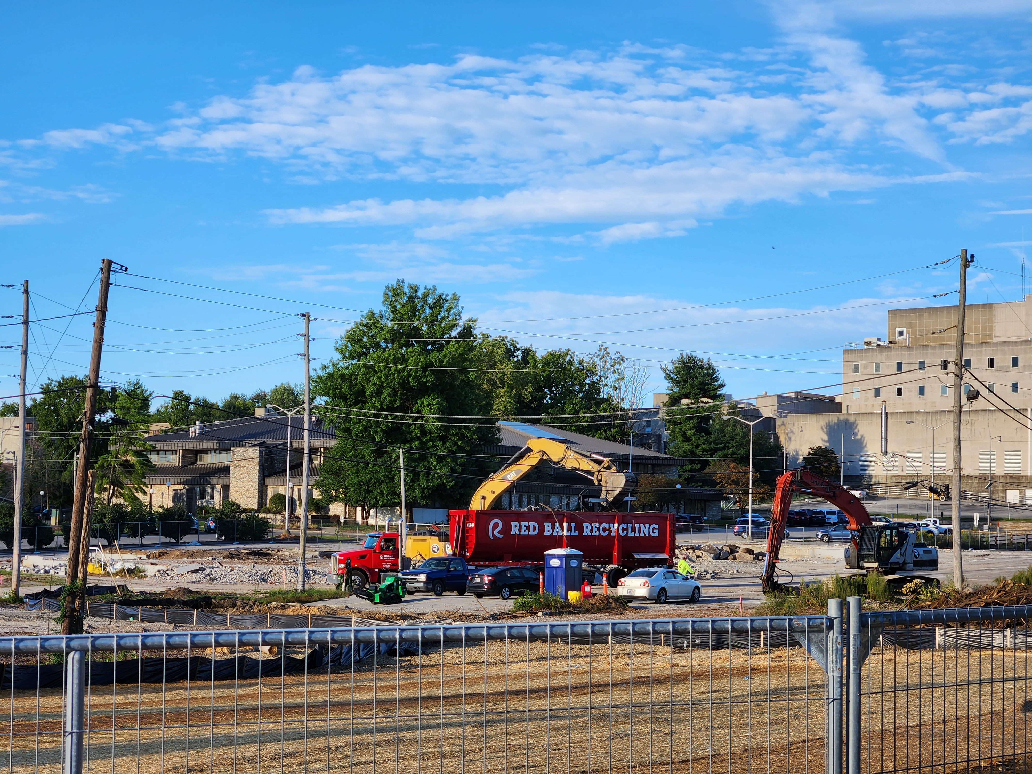 Behind a construction fence demolition materials are being salvaged and placed in an industrial recycling truck.