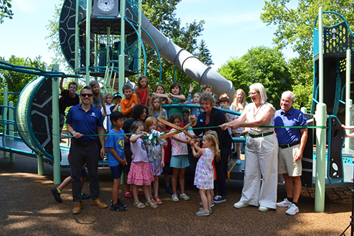 Bryan Park Playground ribbon cutting with Mayor Thomson, Deputy Mayor Knapp, and Bloomington-area children cut a green ribbon with giant scissors