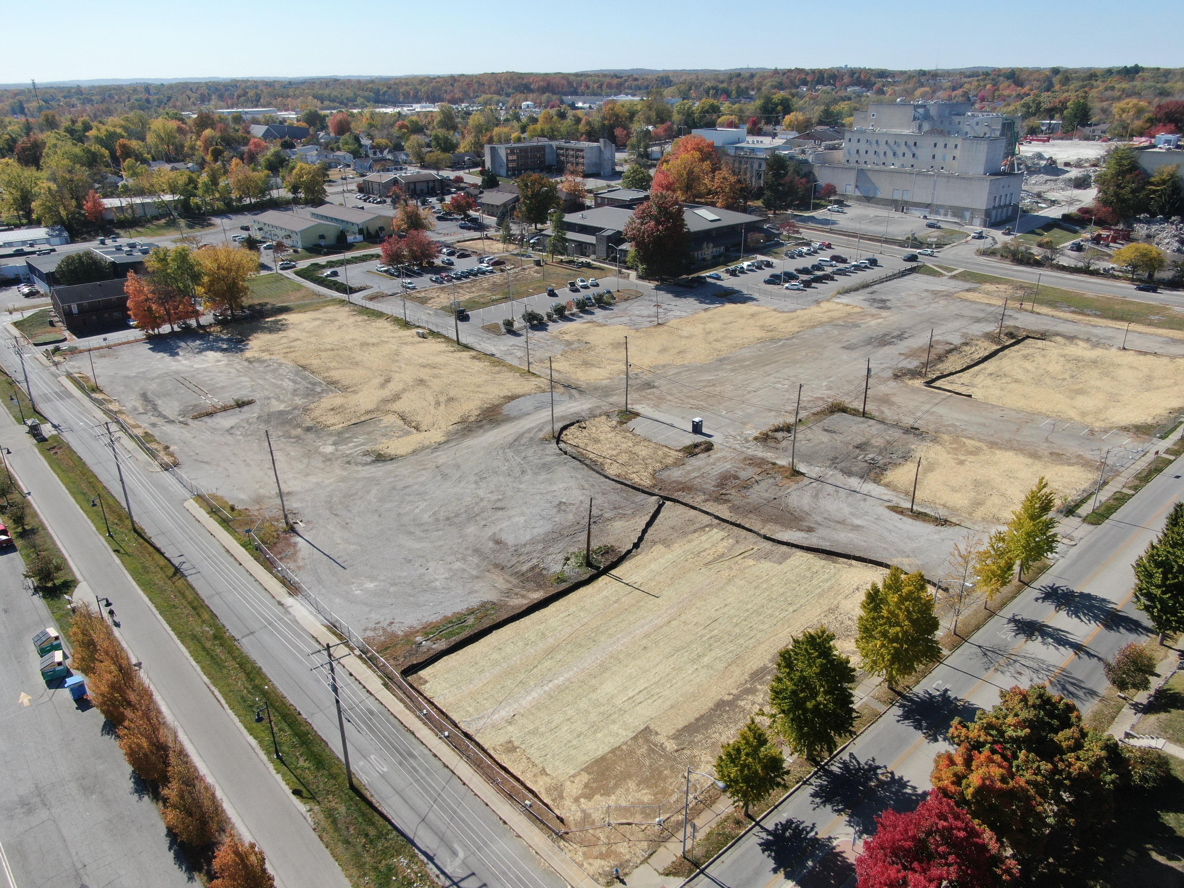 The right photo is looking southwest from the intersection of 2nd and Morton Street, the site is covered in straw with black silt fence surrounding it, and the legacy hospital can be seen in the background.