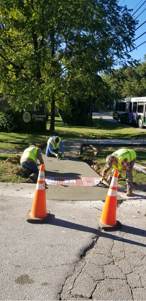 Three City workers in reflective safety vests install an ADA-compliant curb ramp on S Walnut Street Pike. 
