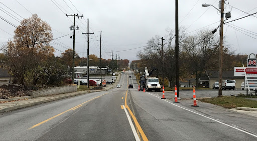 Photo shows 17th Street looking west. Orange and white traffic channelizers are on the north side of the street as is a work vehicle.