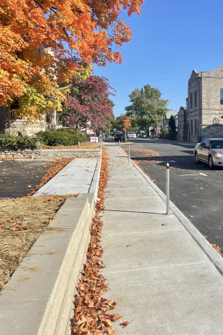 Image shows a sedan drives south on Grant between Longfei Restaurant and Soma Coffeehouse. Fall leaves line the sidewalk. 