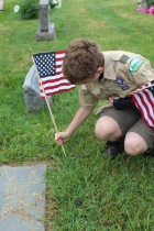 Scout placing American flag on grave of veteran