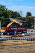 Behind a construction fence demolition materials are being salvaged and placed in an industrial recycling truck. 