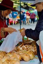 A woman farm vendor places a whole yellow onion into a plastic shopping bag for a Market customer. Photo by Merrill Hatlen.